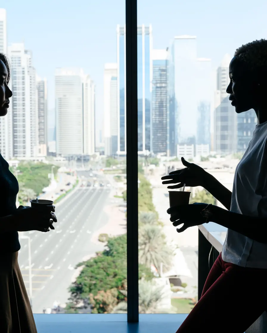 Two colleagues talking over coffee beside a city window