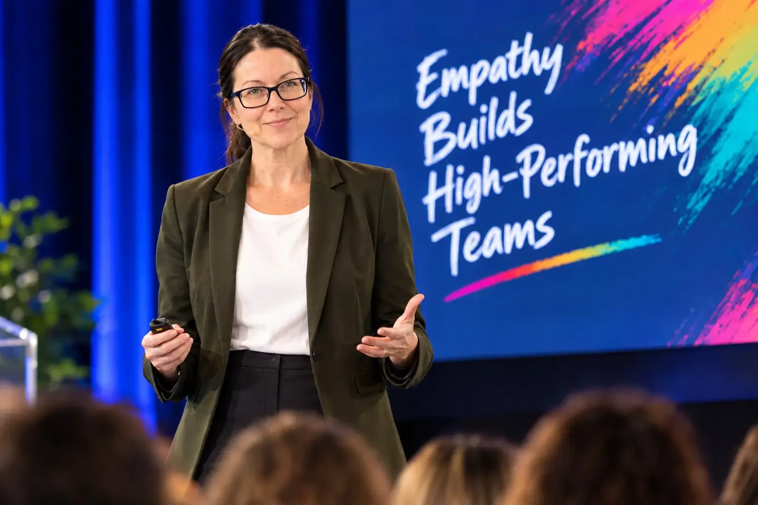 Jennifer Collymore presenting on stage, with a slide reading Empathy Builds High-Performing Teams behind her