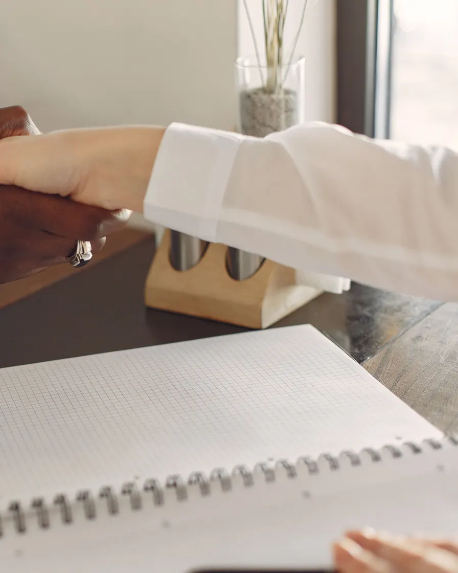 Two people shaking hands across a desk during a job interview